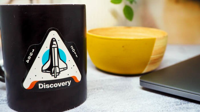 Die cut white vinyl sticker with discovery design applied to a black mug