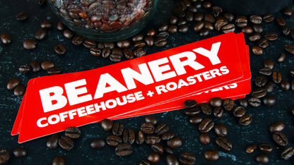 Vinyl logo sticker with Beanery branding amidst coffee beans
