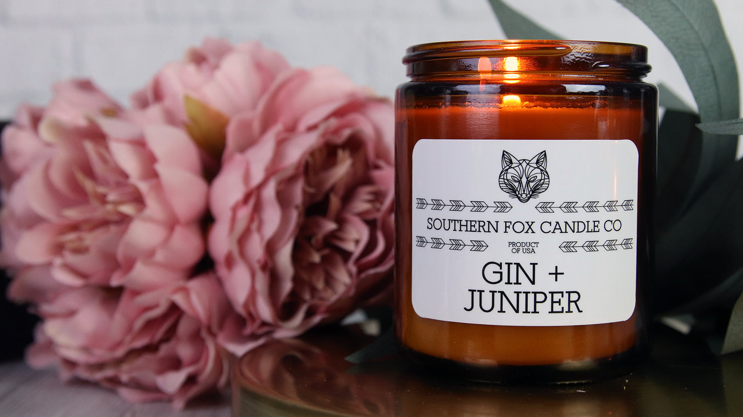 White vinyl candle labels with rounded corners with gin and juniper design applied to an amber candle jar