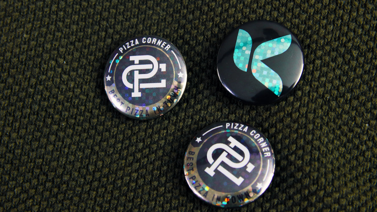 25mm (1-inch) custom glitter button badges with different designs pinned to soft fabric using pin backing