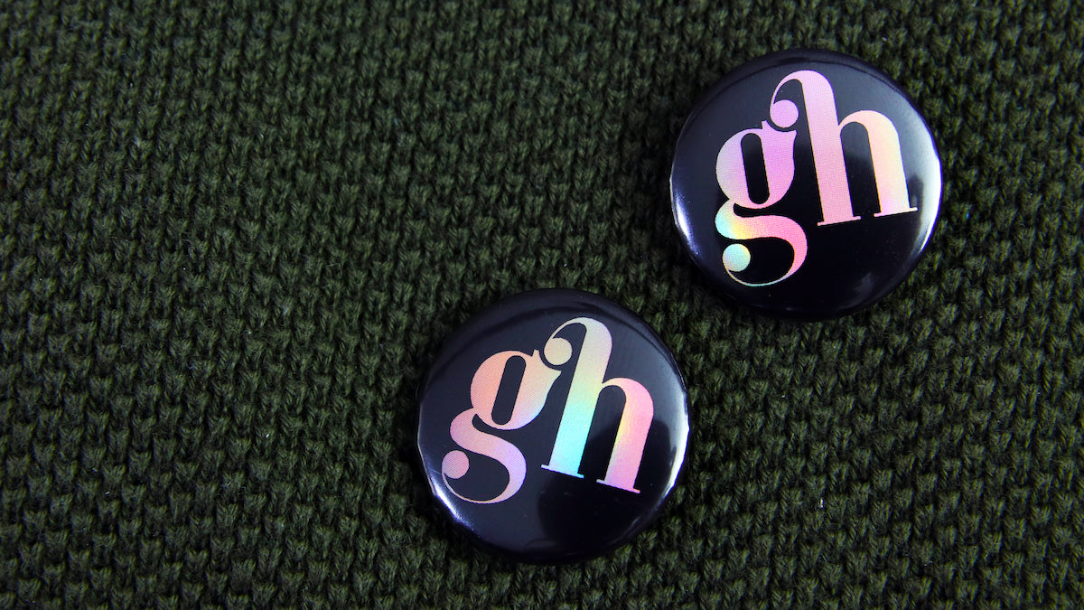 25mm (1-inch) holographic button badges printed with GH logo pinned to a bag