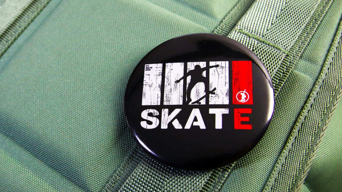 58mm (2.25-inch) Skate logo button badge pinned to a green bag