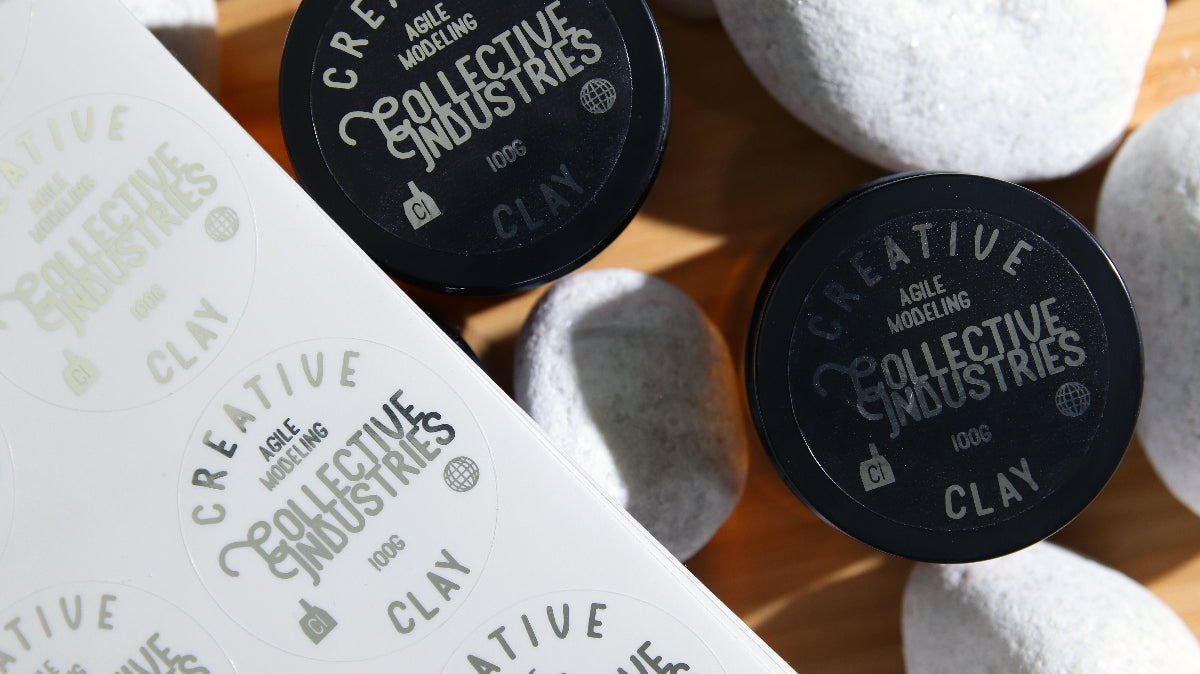 Circle eco-friendly silver foil label with modelling clay design applied to black tins next to sheets of labels