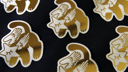 Die cut eco-friendly gold foil stickers with star cat design against a black background