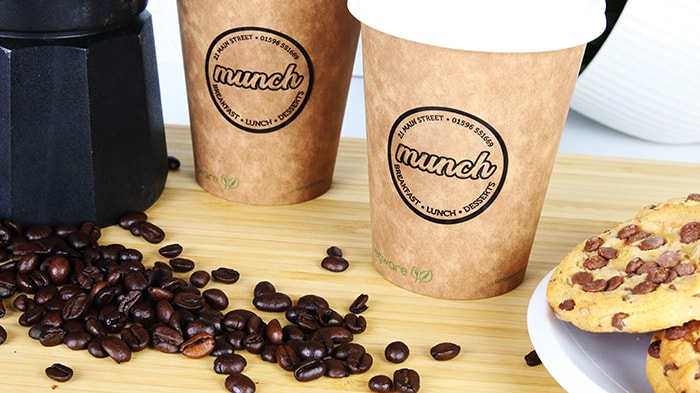 Round clear eco friendly stickers with munch design applied to brown paper coffee cups