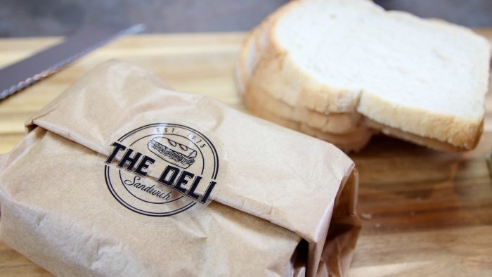 Circle eco-friendly clear bakery labels with a deli logo applied to seal a sandwich wrap