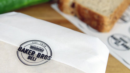 Clear eco-friendly label round with Baker Bros logo applied to seal a sandwich wrapper
