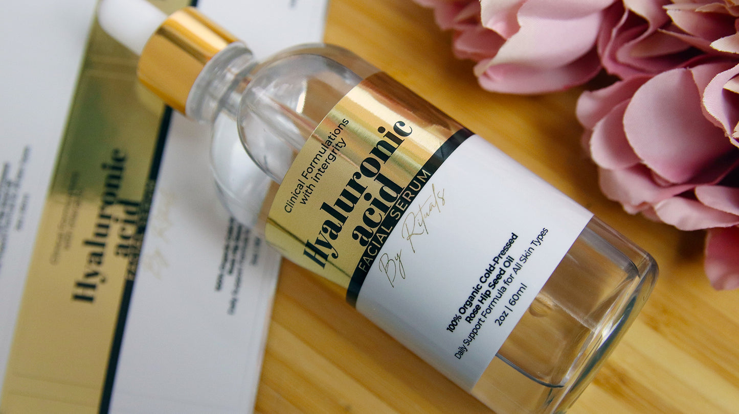 Gold business label with hyaluronic acid facial serum logo applied to a clear cosmetics bottle next to sheets