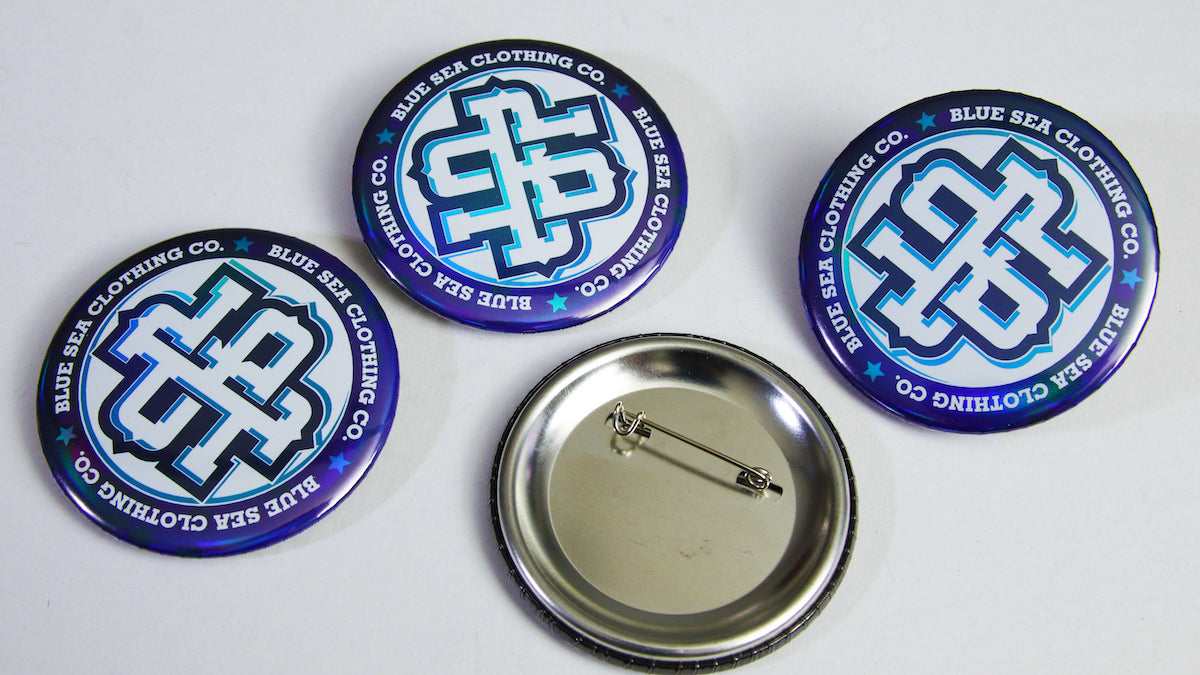 Large 58mm (2.25 inch) Blue Sea designs on holographic badges on a table