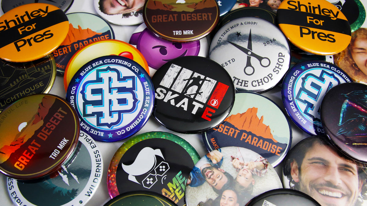 Loads of large 58mm (2.25") custom printed buttons and badges scattered on a table