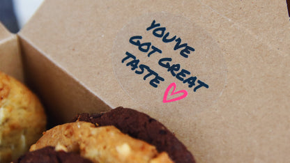 Oval clear bakery labels applied to a cardboard box filled with cookies stating you've got great taste