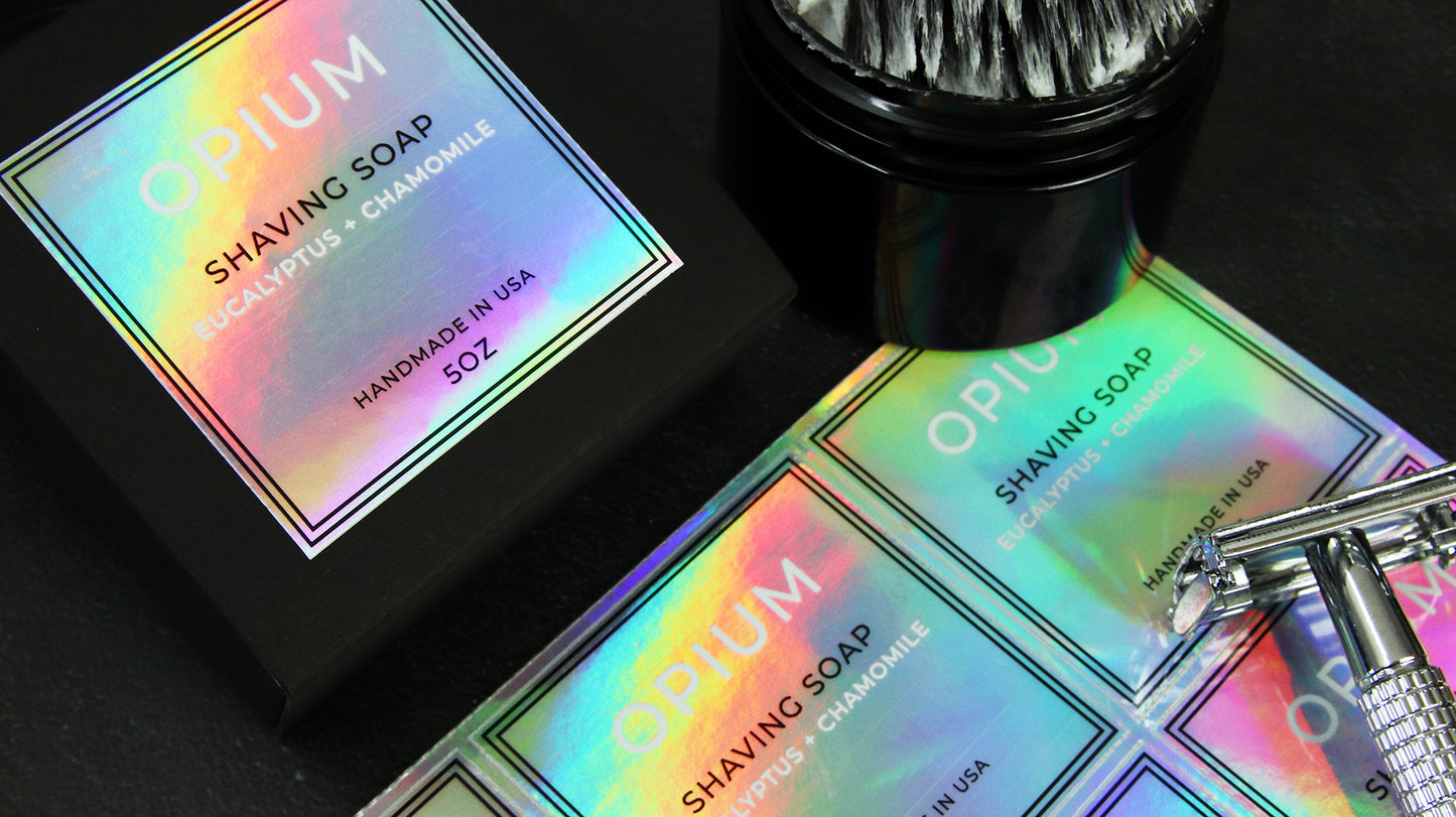 Square holographic label applied to black soap box next to shaving tools