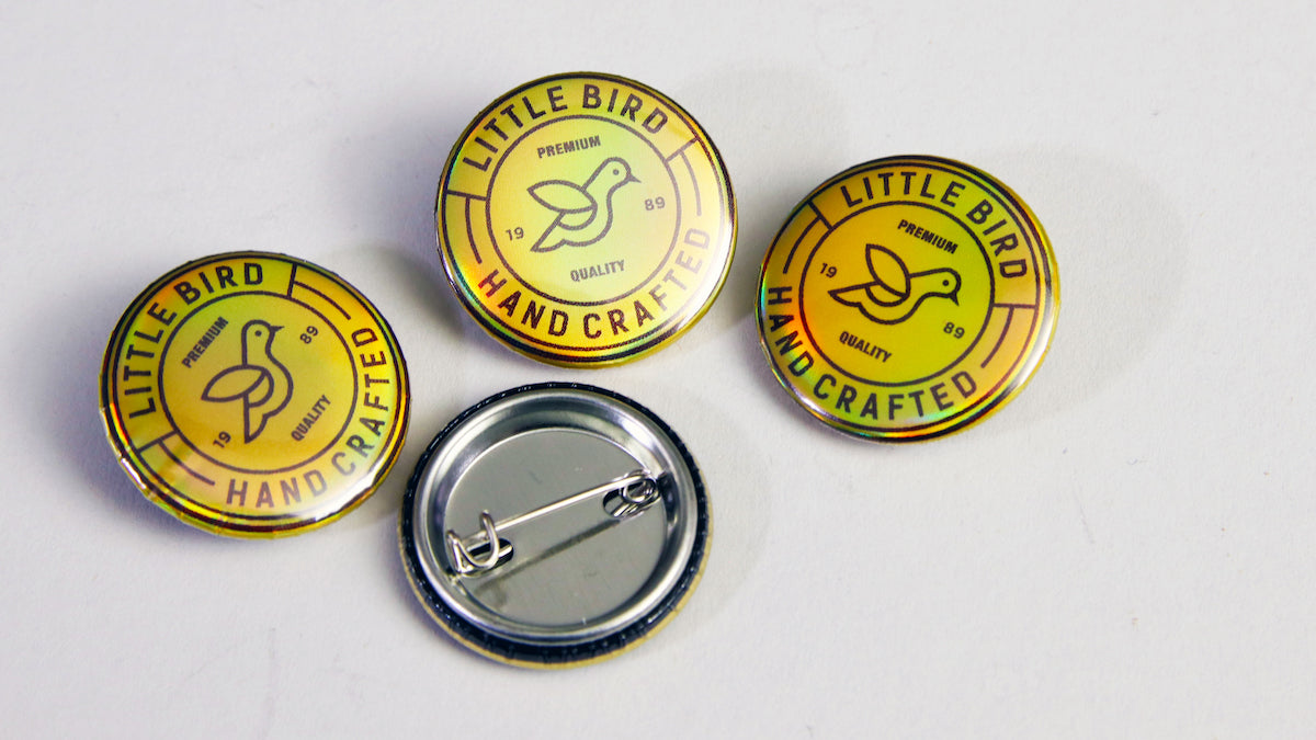 Yellow and black little bird logo on a holographic button badge 25mm small