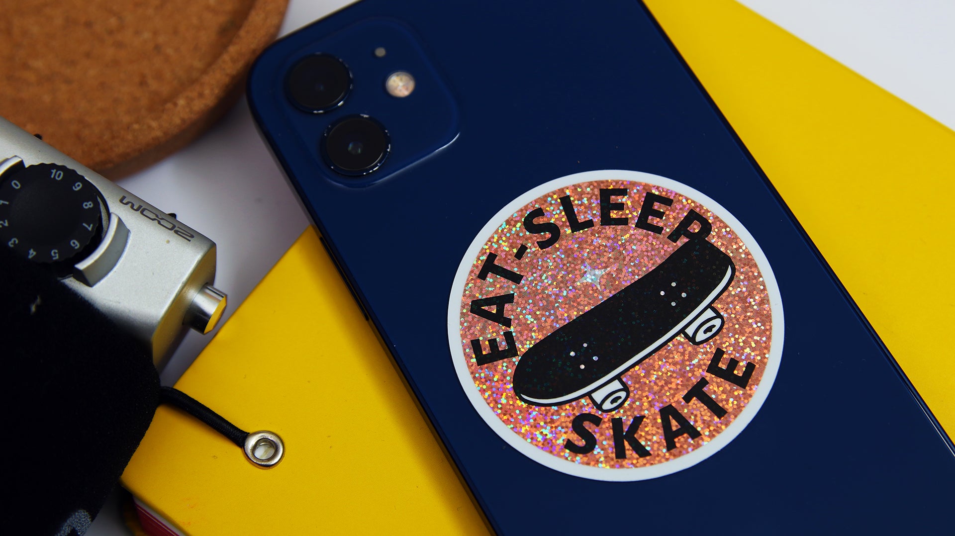 Circle eco-friendly glitter sticker with skate design applied to a blue iPhone
