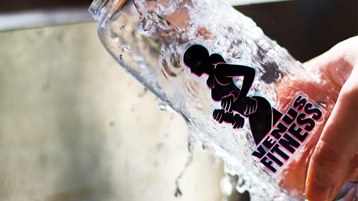 Clear die cut sticker applied to a water bottle held under a tap with running water