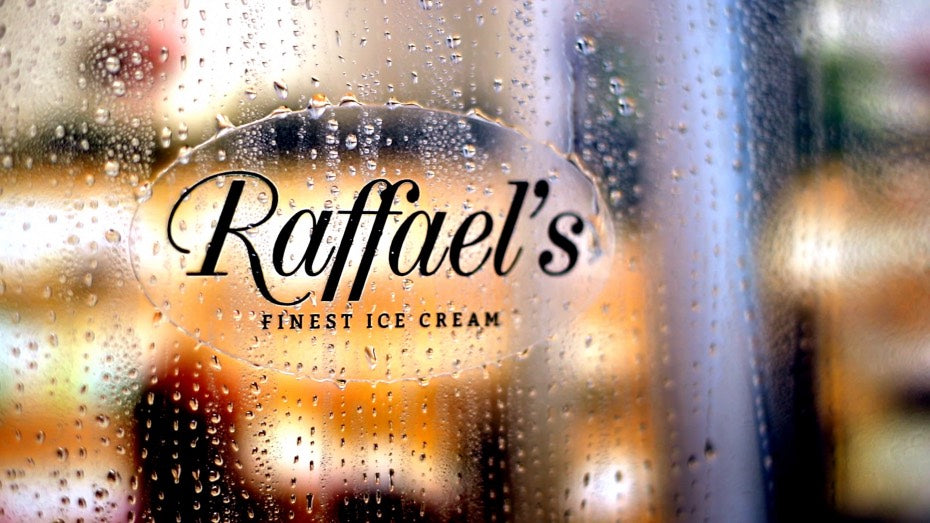 Clear oval waterproof label with raffael's logo applied to a glass door with rain dropping off