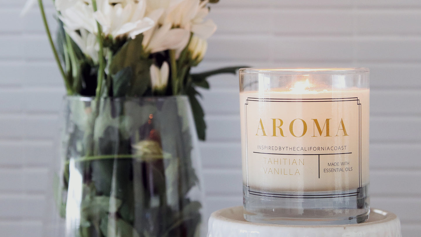 Clear rounded corner candle labels apply to a clear candle jar with a white candle next to white flowers in a vase