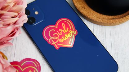 Eco-friendly holographic die cut sample in the shape of a heart with a girl power logo applied to a blue phone