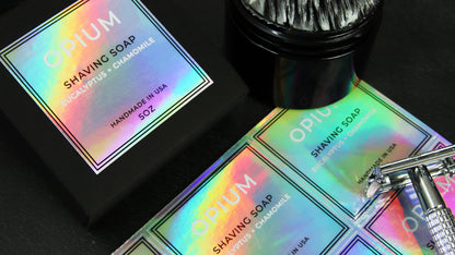 Eco-friendly holographic labels applied to black soap box next to shaving tools and sheets