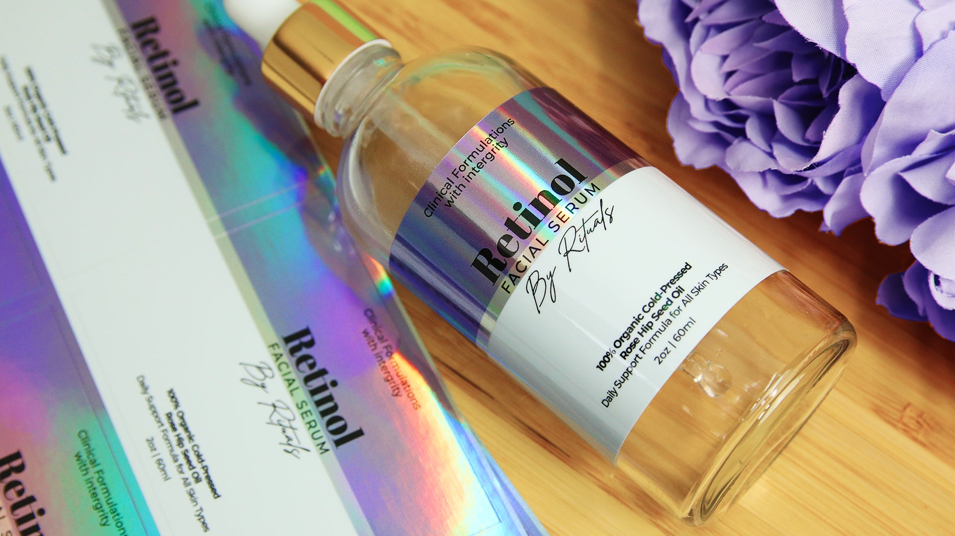 Eco-friendly holographic labels with retinol facial serum logo applied to a clear cosmetics bottle next to sticker sheets