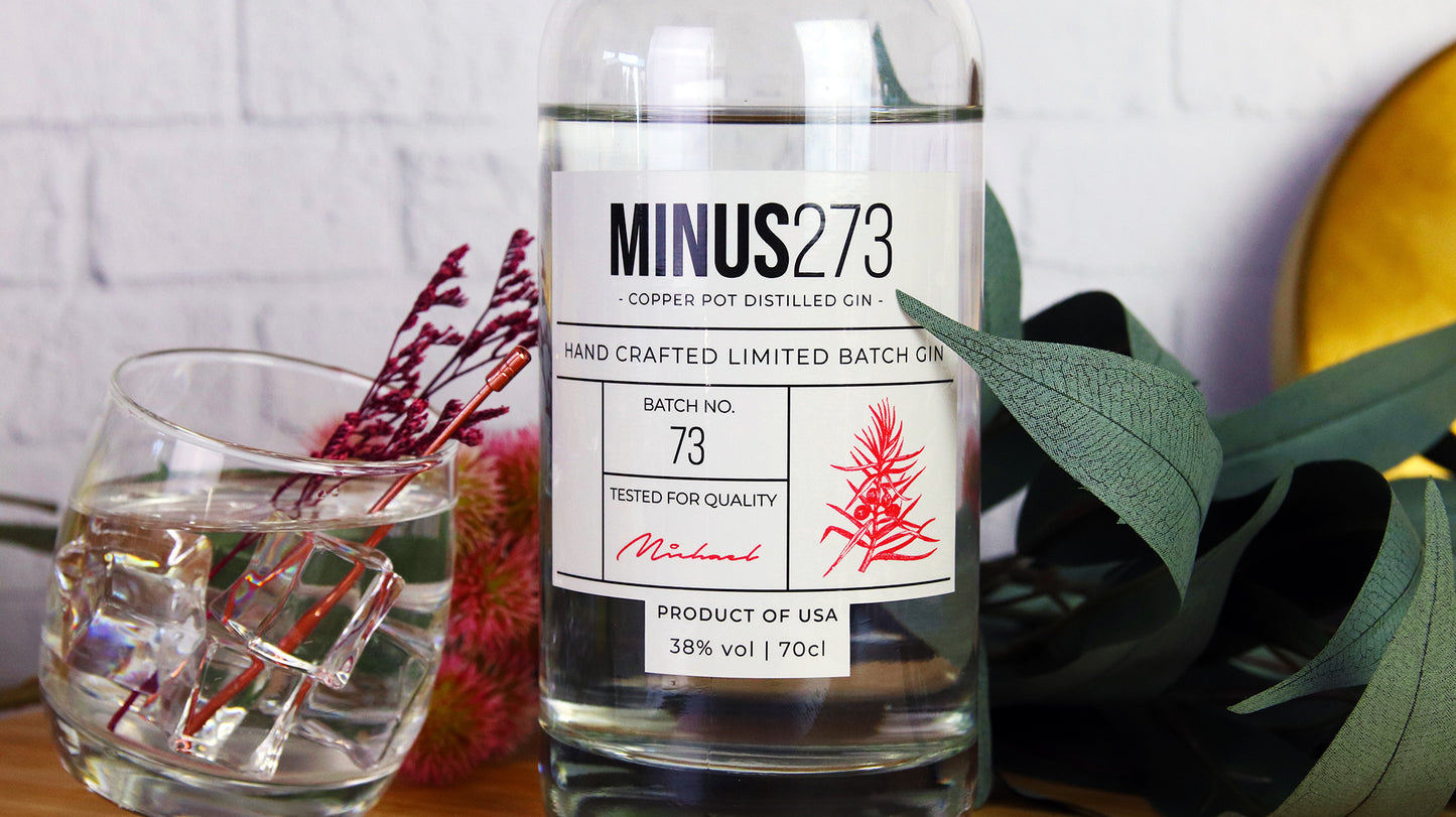 Eco friendly label applied to glass gin bottle next to a tilted glass filled with a cocktail