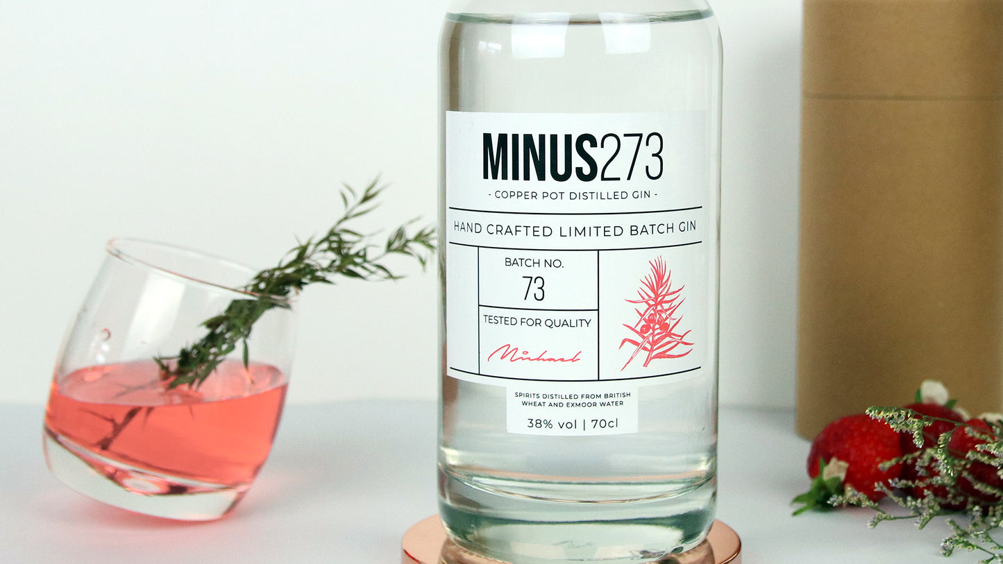 Labels applied to glass gin bottle next to a tilted glass filled with a cocktail