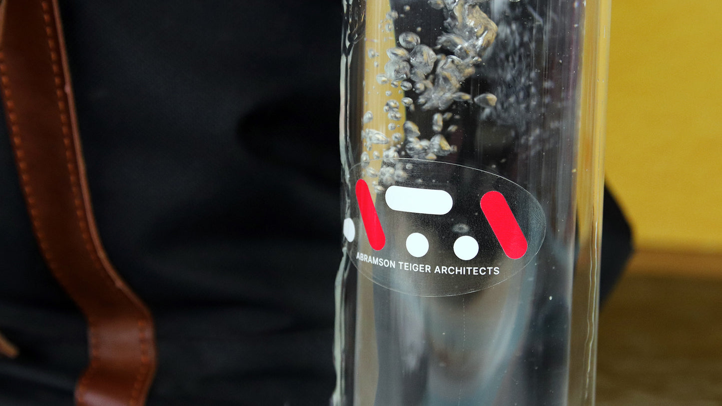 Oval clear logo sticker applied to clear water bottle next to a backpack