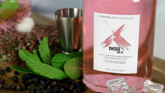 Rectangular clear gin label applied to a pink gin bottle next to a measuring cup and mint leaves
