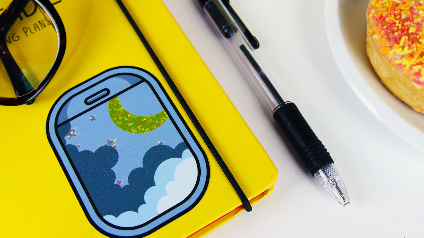 Rounded corner glitter sticker with air plane window design applied to a yellow note book