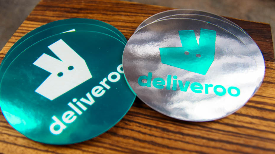 Stack of round mirror silver company labels with deliveroo logo on a table