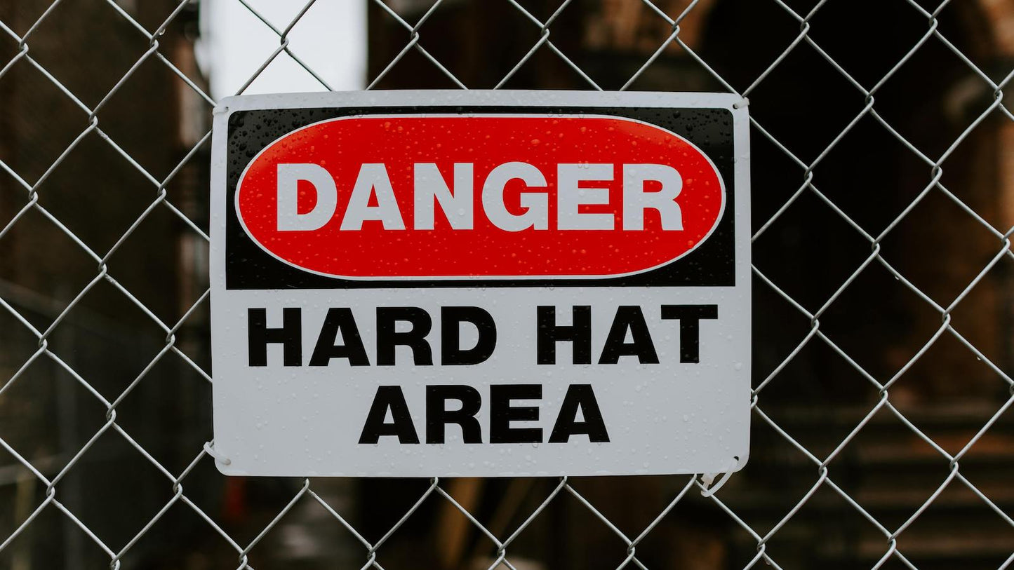 Warning label hard hat area cable tied to a chainlink fence