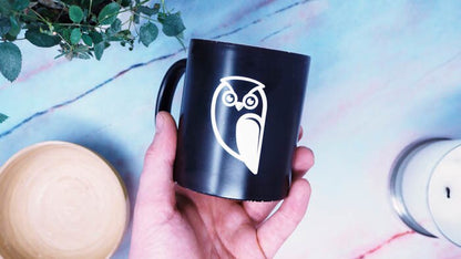 White transfer sample with owl design applied to a black mug