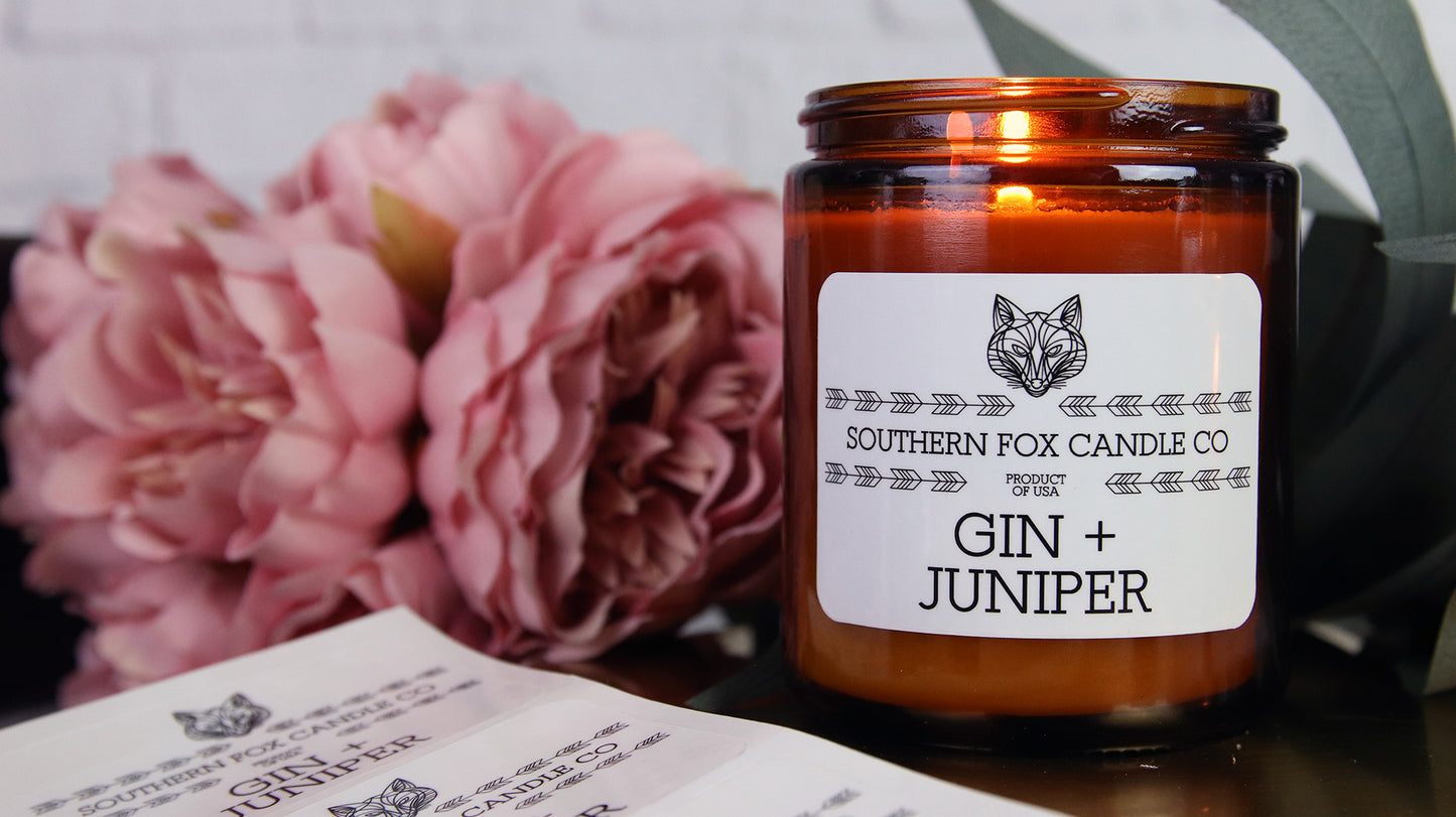 White vinyl candle labels with rounded corners with gin and juniper design applied to an amber candle jar